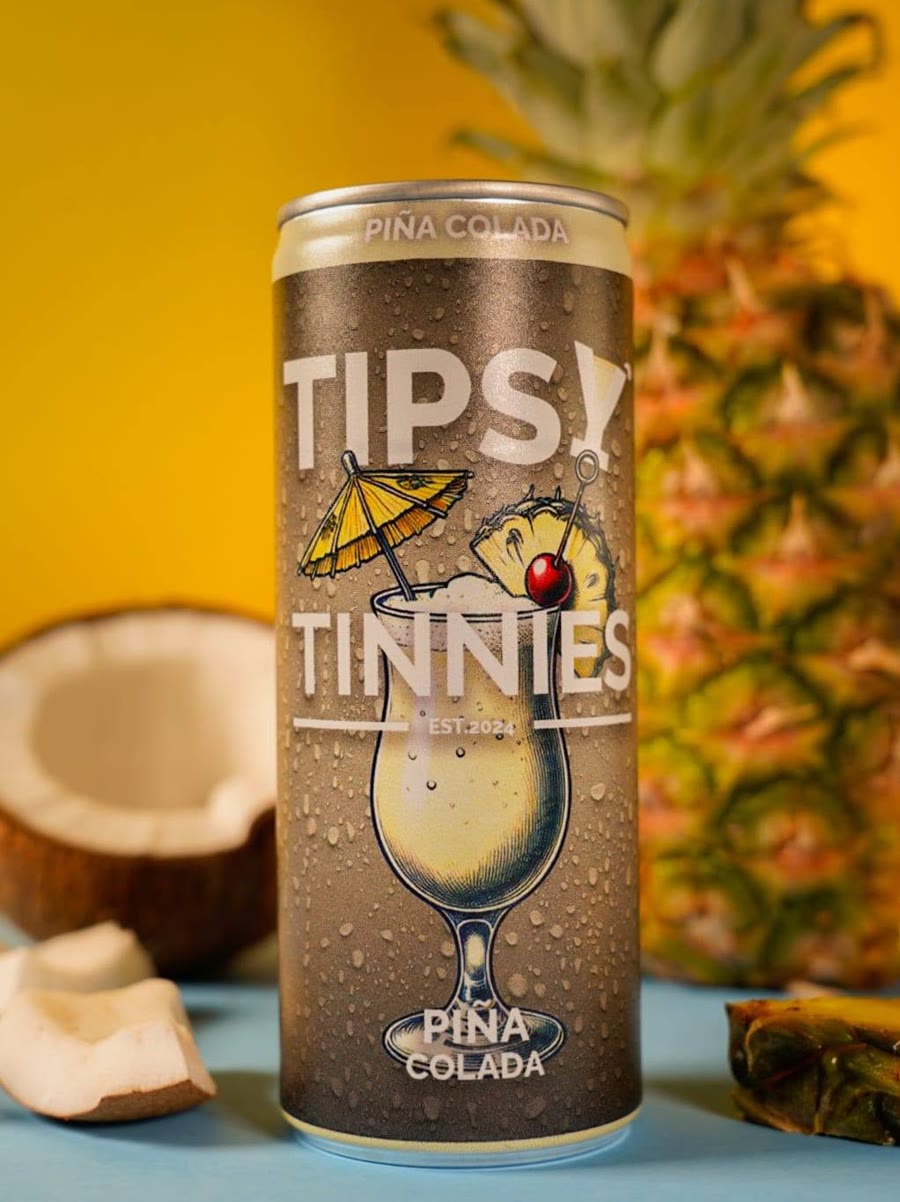 Piña Colada tin in front of a pineapple and a halved coconut