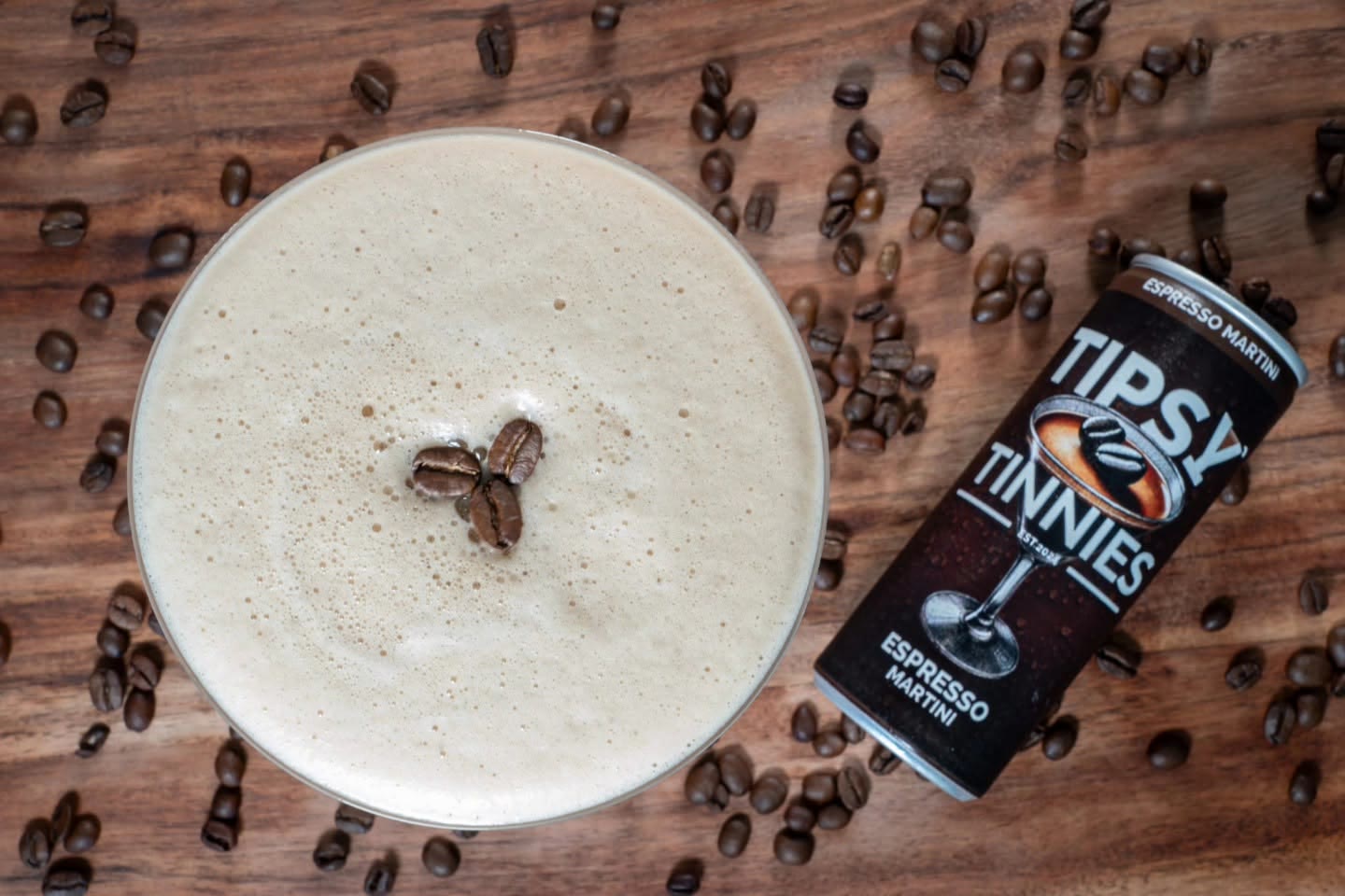 Espresso Martini with three coffee beans on the foam, next to its tin on a wooden bar