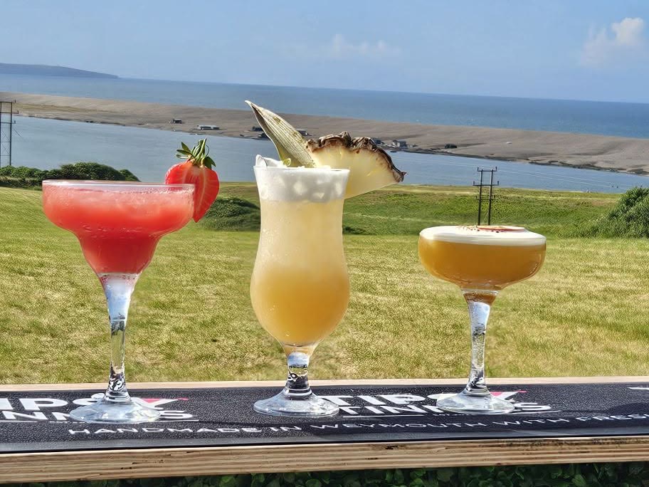 Strawberry Daiquiri, Piña Colada and Pornstar Martini lined up on a bar overlooking Weymouth Bay