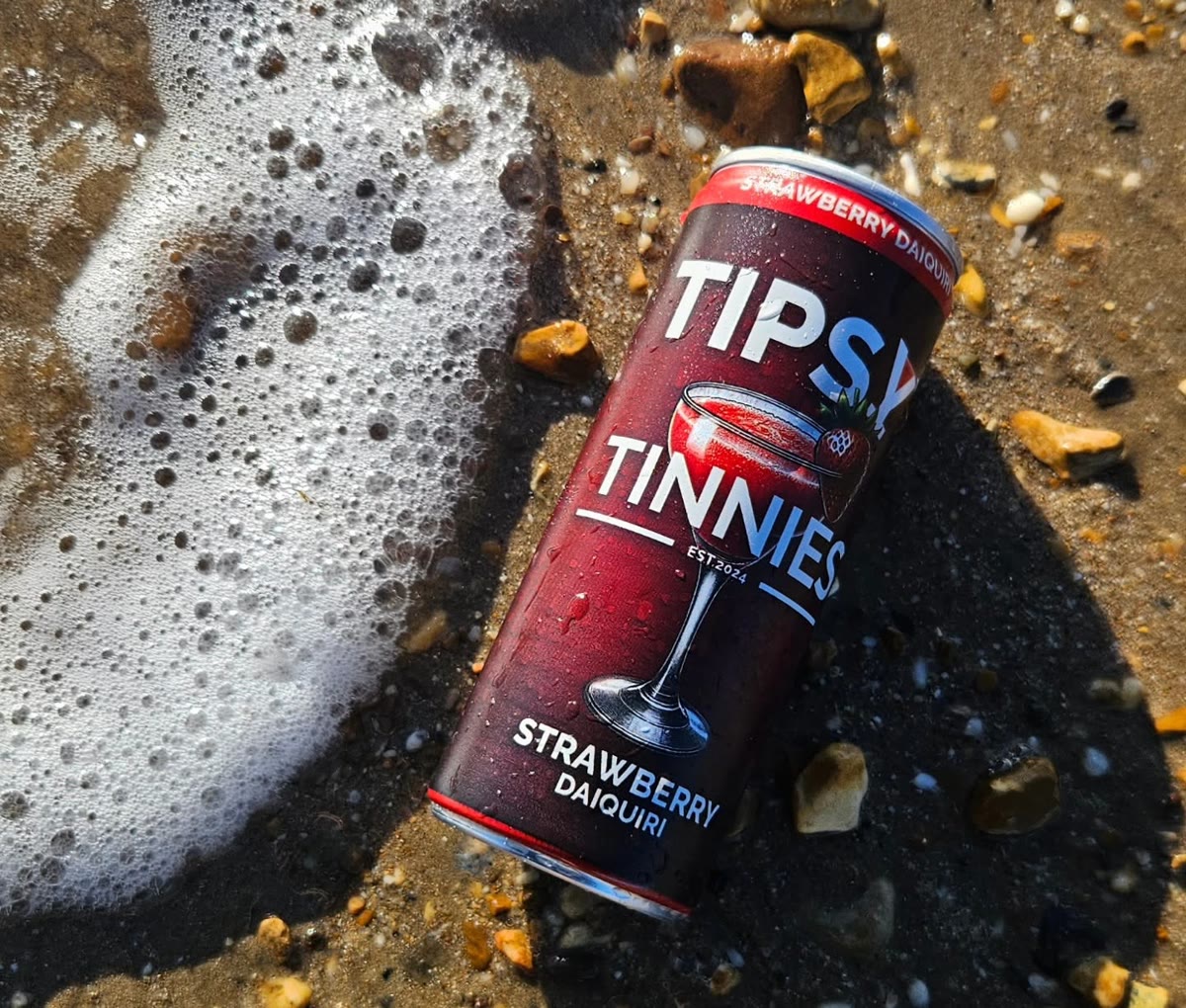 Strawberry Daiquiri tin lying on the wet sand at the water's edge